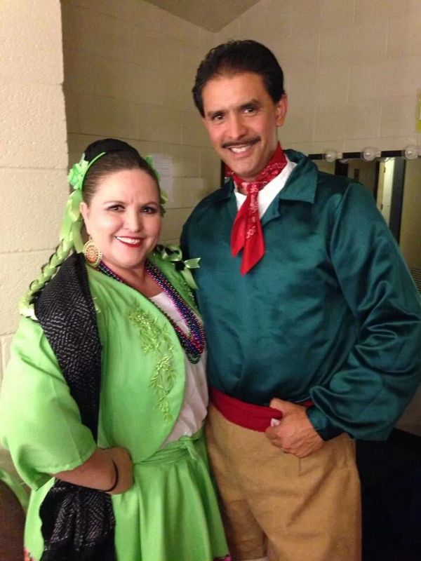 A smiling couple dressed in traditional Mexican folkloric costumes.