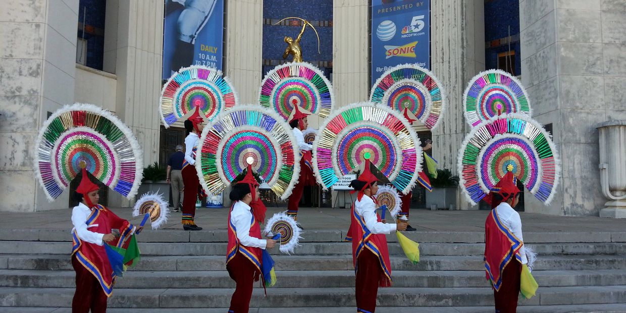 Dancers in vibrant traditional attire with large colorful headdresses perform on stone steps.