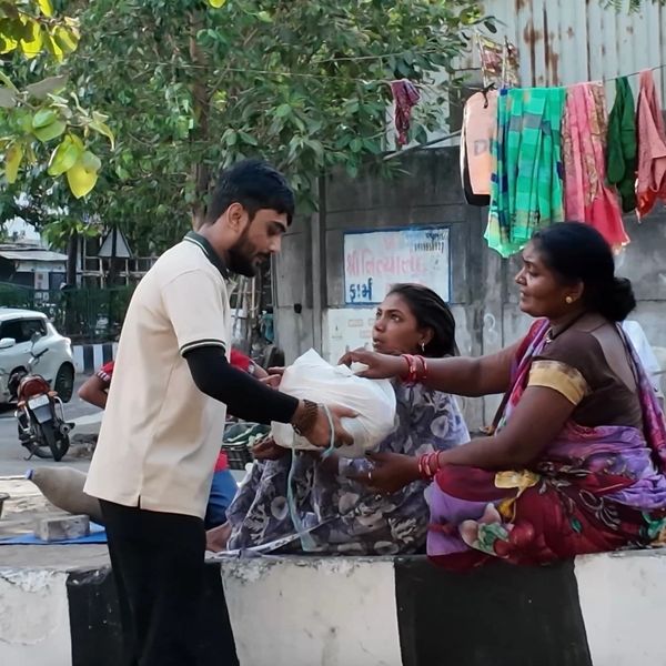 Man handing a bag to two seated women in an outdoor setting.