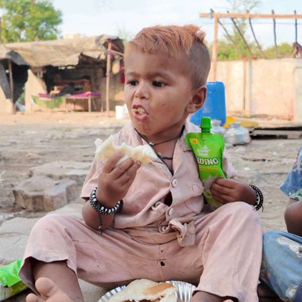 Child eating bread and holding a green food pouch.