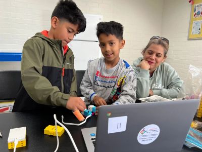 Two boys and a woman engage in a robotics project at a laptop.