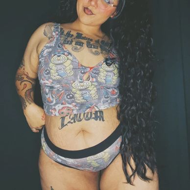 Person with long curly hair in cartoon-printed underwear and multiple tattoos.