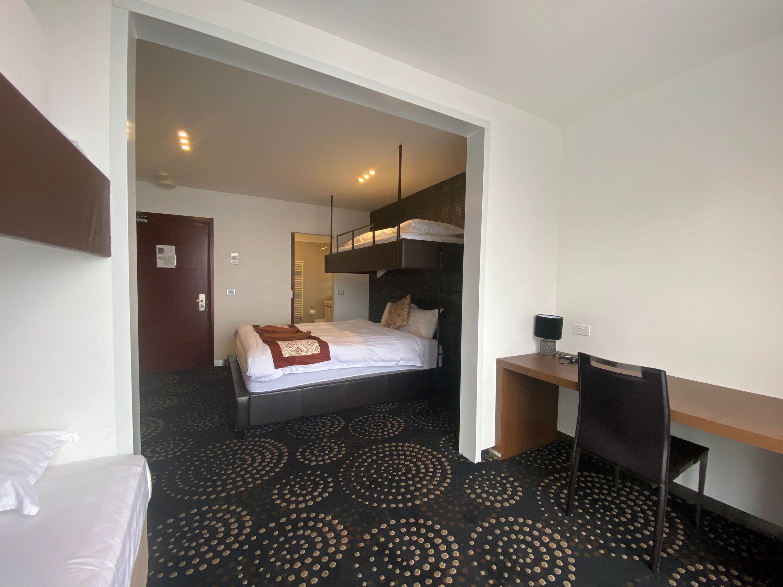Modern hotel room with a unique loft bed and patterned carpet.
