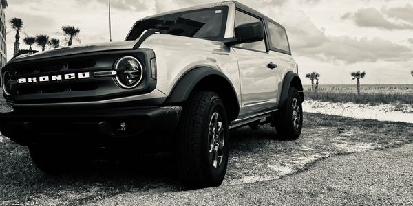 A Ford Bronco parked near a beach under a cloudy sky.