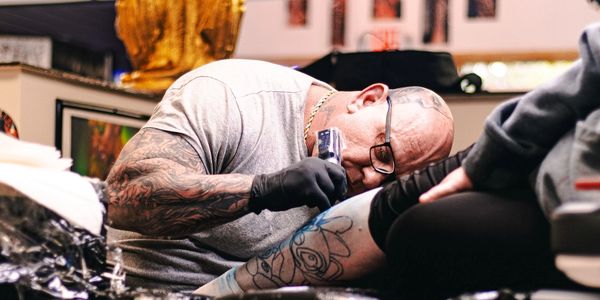 A tattoo artist carefully inks a blue cartoon design on a client's leg.
