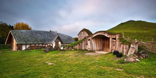Old wooden houses and a grassy hill under a cloudy sky.