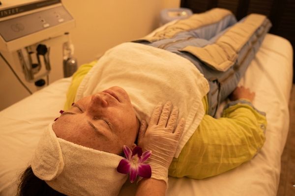 A woman receiving a relaxing facial treatment with warm compresses and a flower.