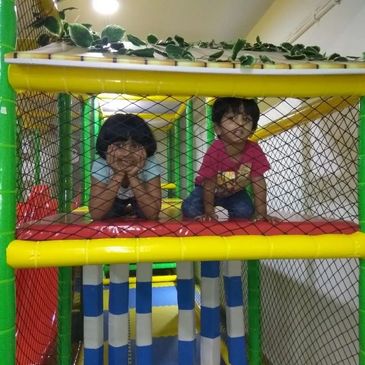 Two children playing inside a colorful indoor playground net structure.