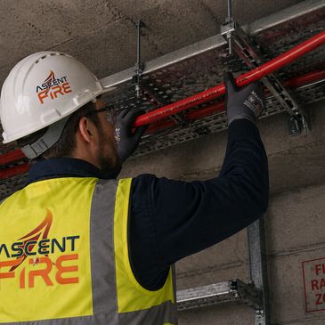 Worker in safety gear installing red piping on ceiling.
