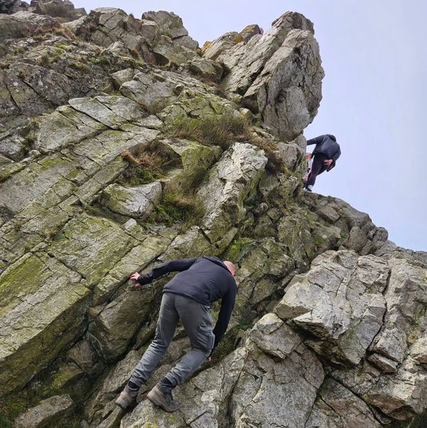 Two people rock climbing a steep, rocky cliff.