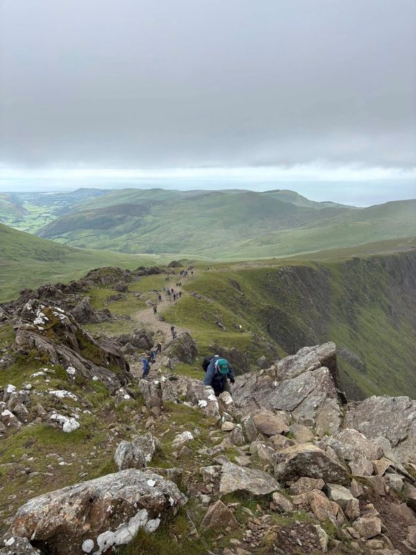 Hikers climbing a rocky mountain ridge under a cloudy sky.