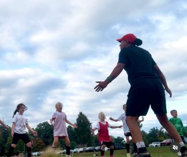 Coach instructing young soccer players during practice under a cloudy sky.