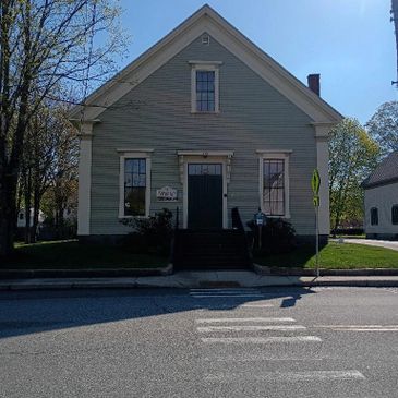 Historic gray wooden building with a central door and symmetrical windows under a clear blue sky.