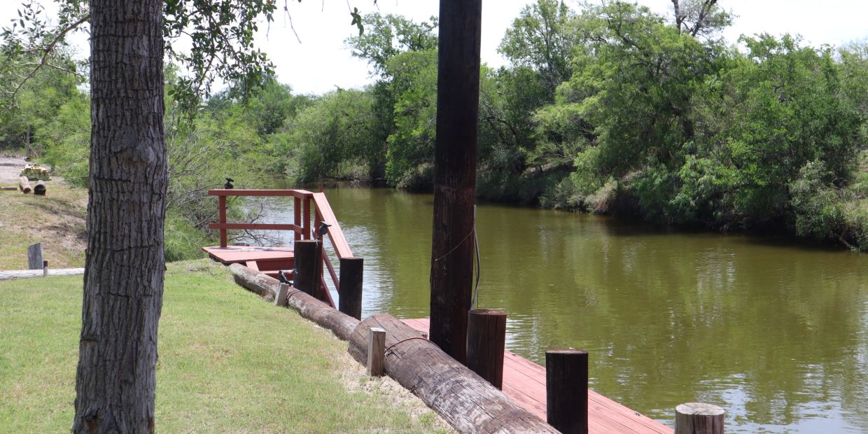 Calm river with wooden dock surrounded by trees.