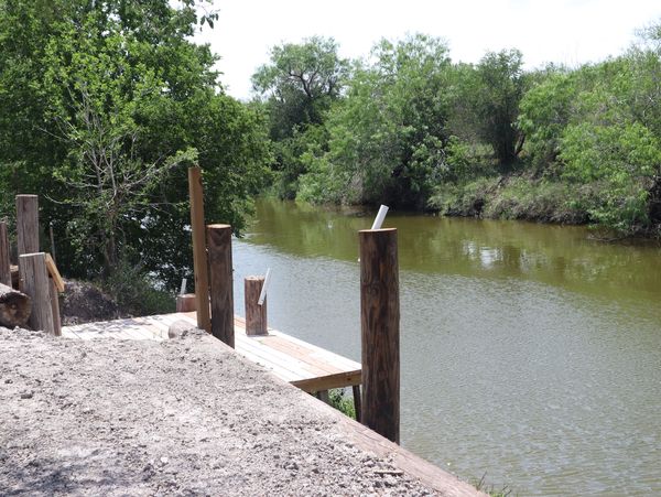 A small wooden dock by a narrow river surrounded by trees.