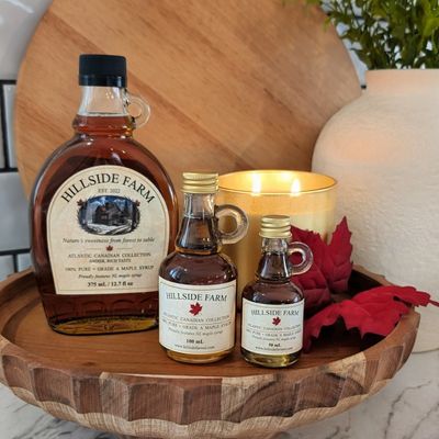 Hillside Farm maple syrup bottles on a wooden tray with a lit candle and decorative leaves.