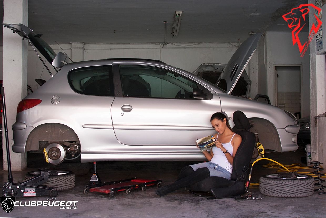 Mujer leyendo junto a un coche sin ruedas en un taller.