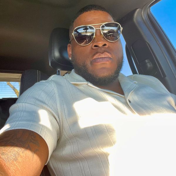 Man wearing sunglasses and a white polo shirt sitting in a car.
