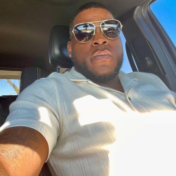 Man wearing sunglasses and a white polo shirt sitting in a car.