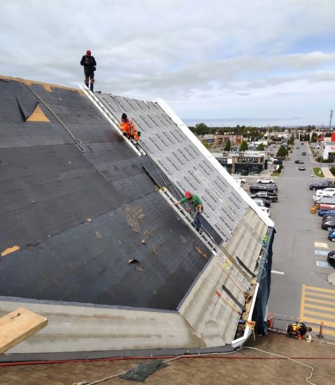 Workers use ladders on a steep roof for roof replacement