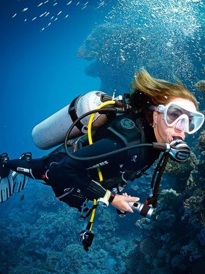 A scuba diver explores underwater with a flashlight among coral reefs.