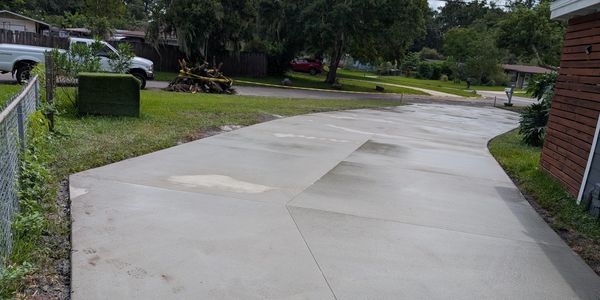 Freshly poured concrete driveway with some footprints and a pile of brush in the background.