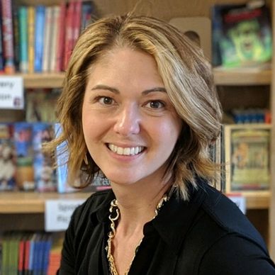 Smiling woman with blonde hair in a bookstore setting.