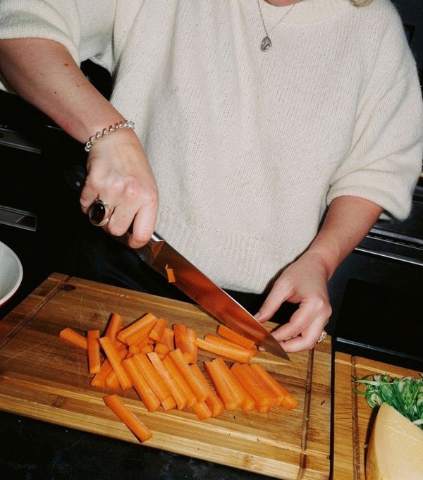 Person chopping carrots on a wooden cutting board.
