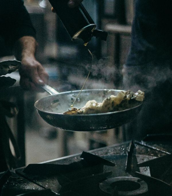 Pouring oil into a sizzling frying pan with food.
