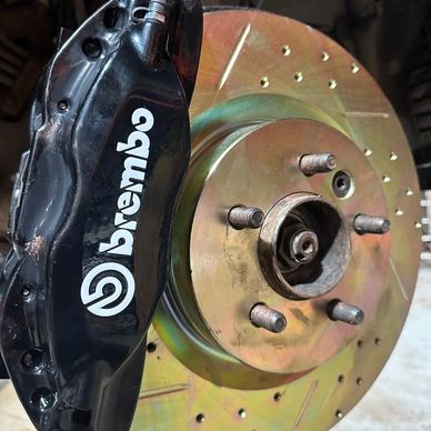 Close-up of a Brembo brake caliper and drilled brake rotor on a vehicle.