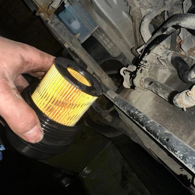 Hand holding a used yellow oil filter near a vehicle engine.