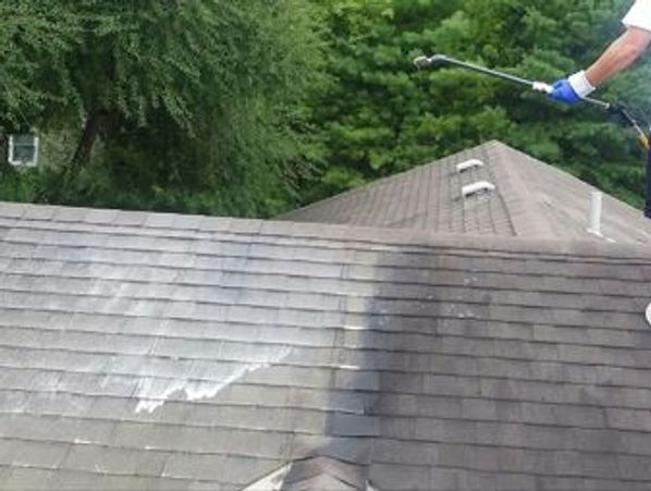 Person pressure washing roof shingles, cleaning dirt and grime.
