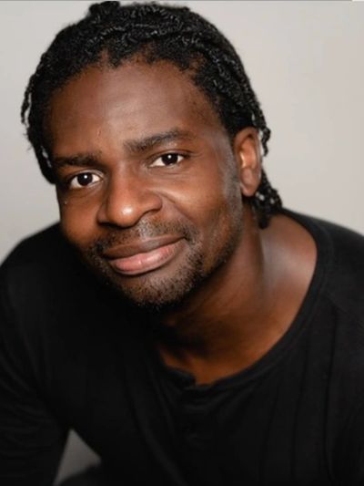 Man with braided hair and black shirt smiling.
