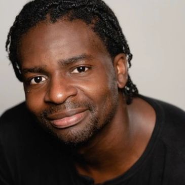 Smiling man with braided hair and a black shirt.