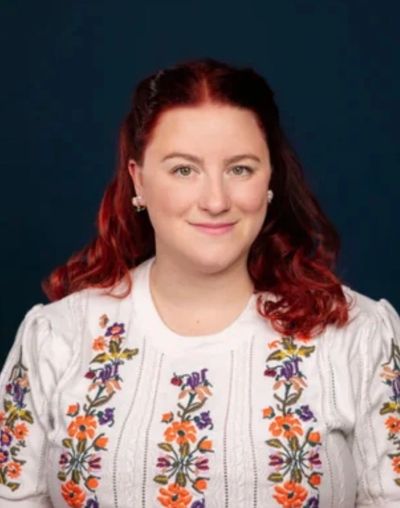 Woman with red hair in a floral embroidered blouse.