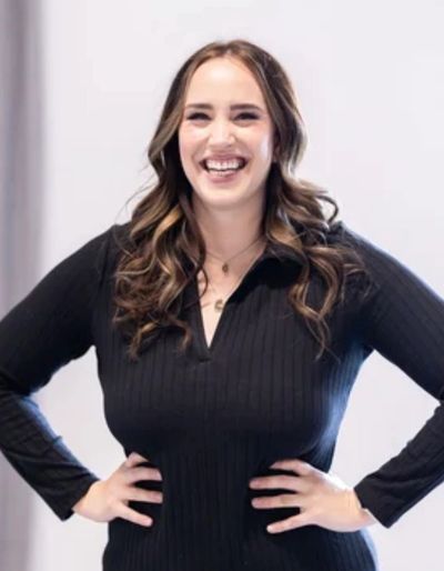 Smiling woman in black dress with hands on hips.