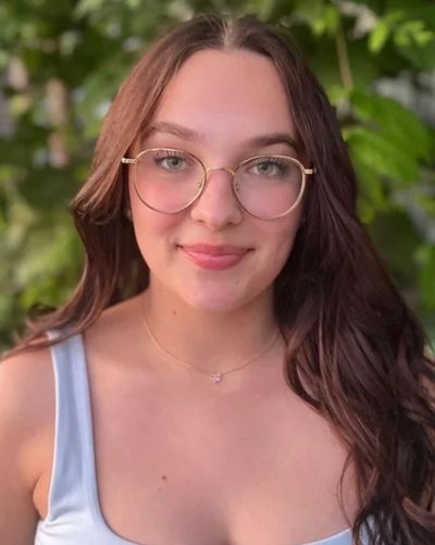 Young woman with glasses smiling outdoors.