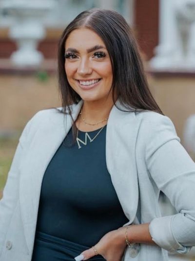 Smiling woman wearing a light gray blazer and dark top.