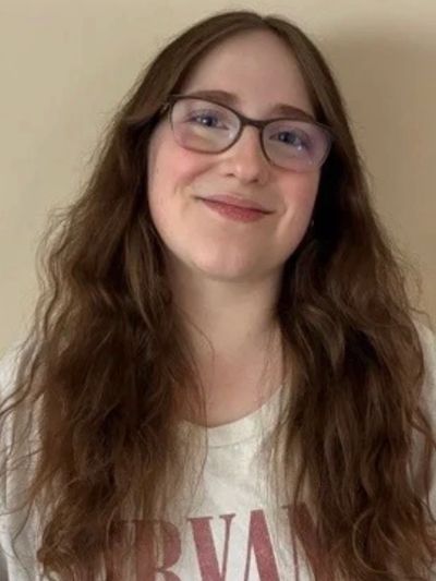 Woman with long hair smiling, wearing glasses.