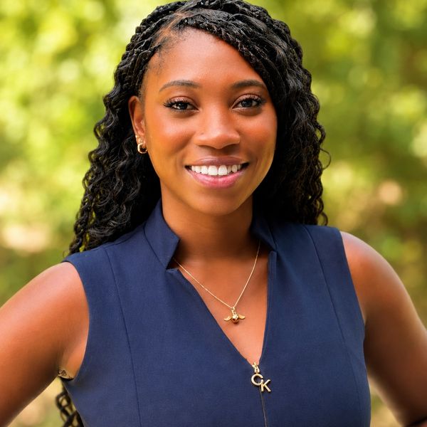 Smiling woman with braided hair wearing a navy blue sleeveless top outdoors.