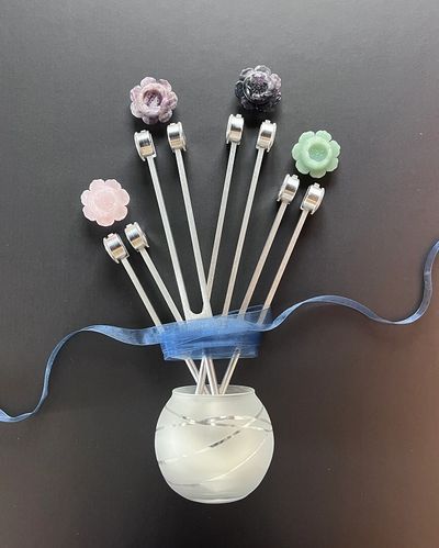 Decorative bottle with flower-topped sticks and blue ribbon.