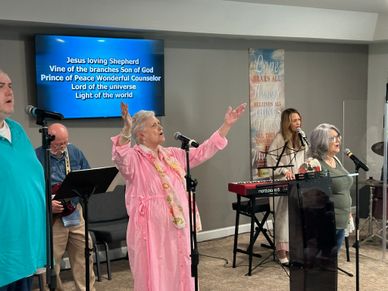 A group worships with raised hands, singing lyrics projected on a screen.