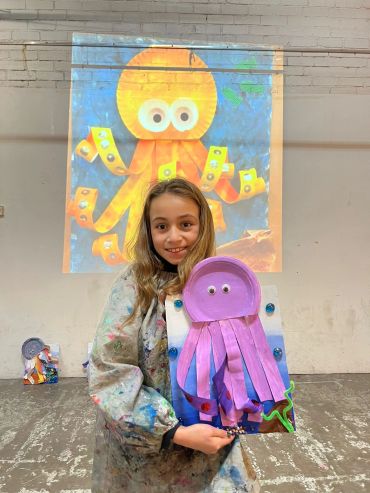 Girl holding a jellyfish craft with an octopus image behind her.