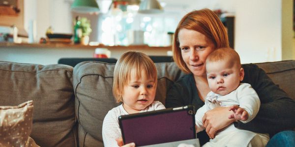 Image of a mother and two children using an ipad on a sofa.