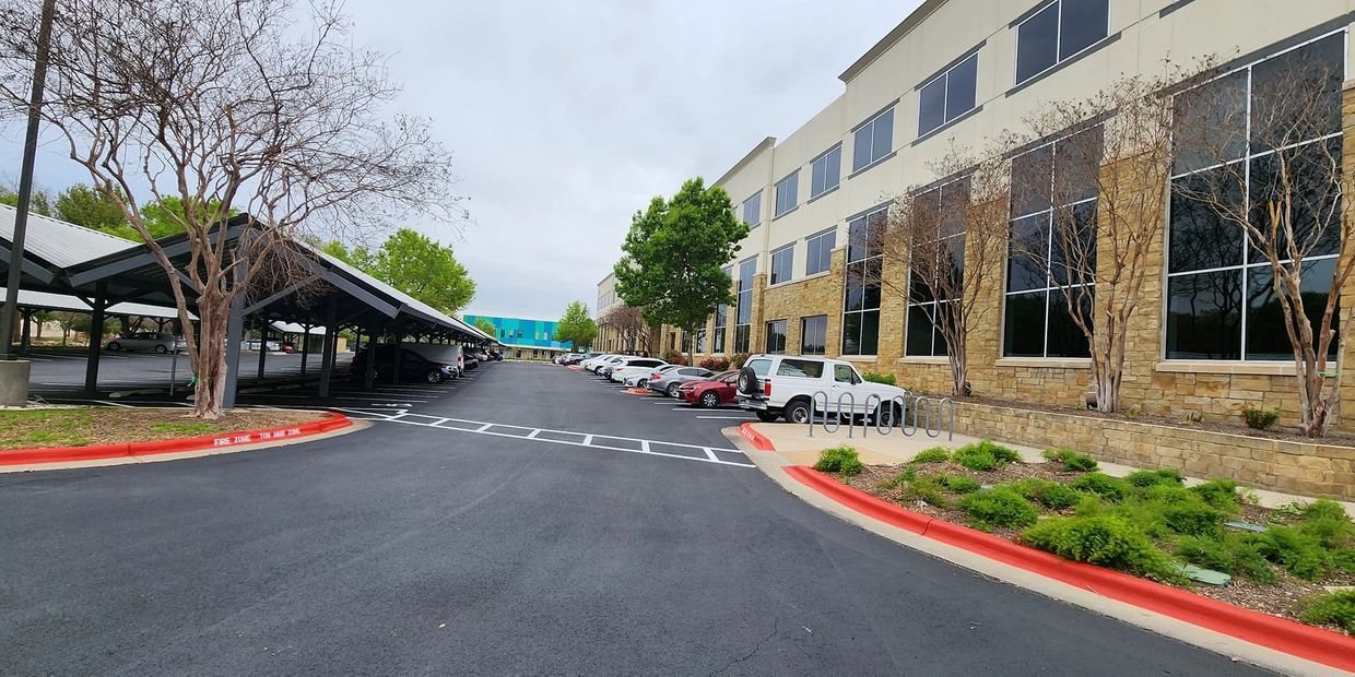 Office building with adjacent parking lot and covered parking area on a cloudy day.