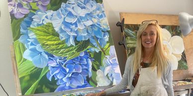 Artist posing with a large, vibrant blue hydrangea painting.