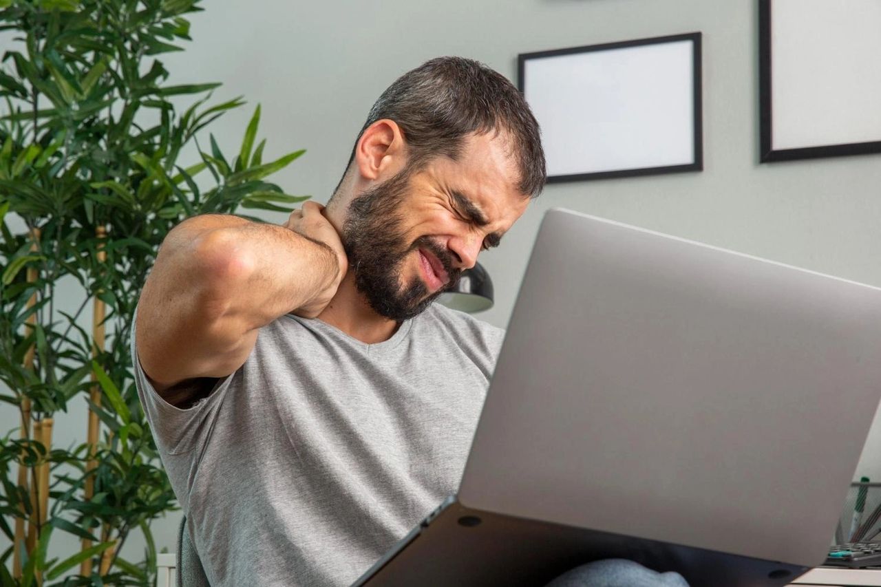 Man experiencing neck pain while working from home on a laptop, highlighting posture strain and the need for natural back pain relief strategies.