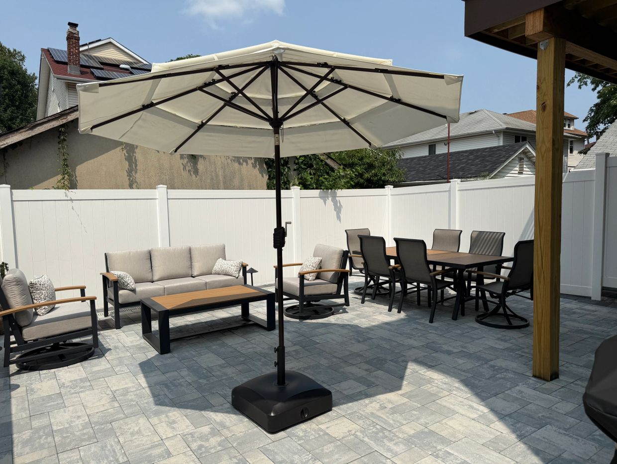 Modern outdoor patio with seating, dining table, and umbrella on a tiled floor. Patio Installation