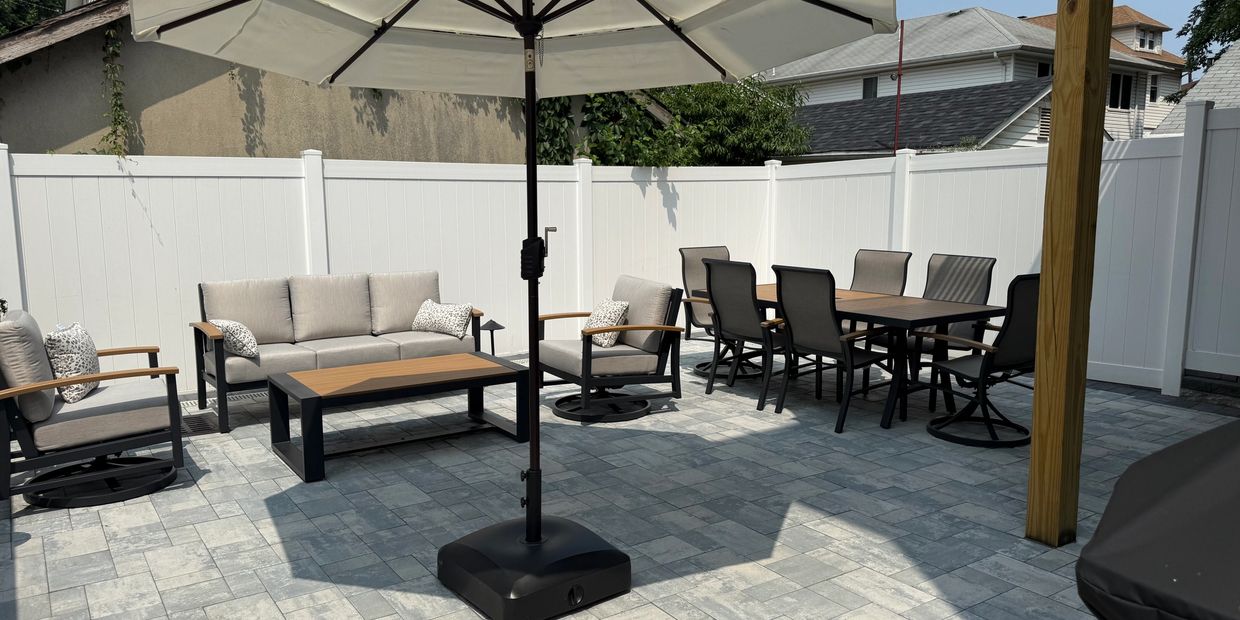 Modern outdoor patio with umbrella, cushioned seating, and dining table on stone pavers.  Expert Hardscape Services in Fort Lee, NJ