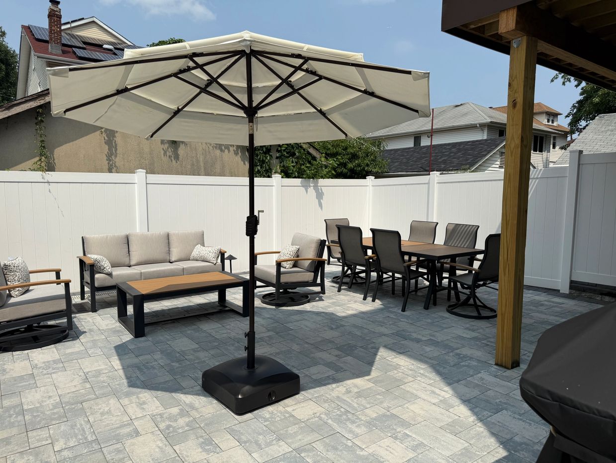 Modern outdoor patio set with umbrella and dining area on stone flooring.
